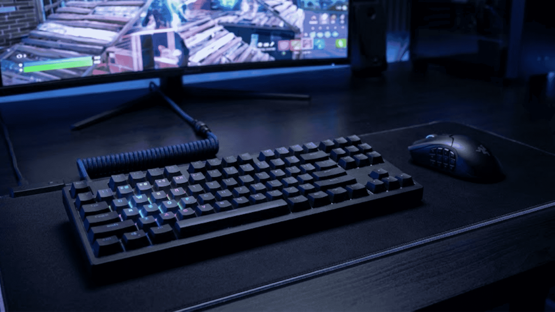 Gaming setup with an illuminated mechanical keyboard and mouse, with a Fortnite build battle on the screen.