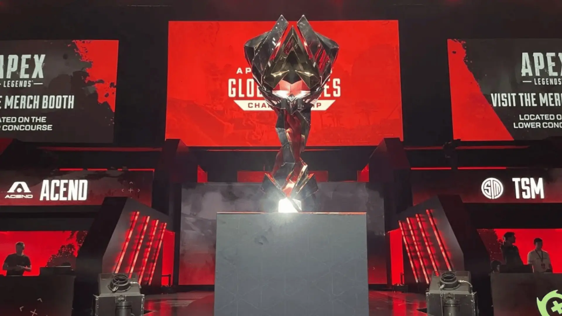 ALGS Championship stage with glowing Apex Legends trophy centered, red esports arena backdrop, team booths and banners