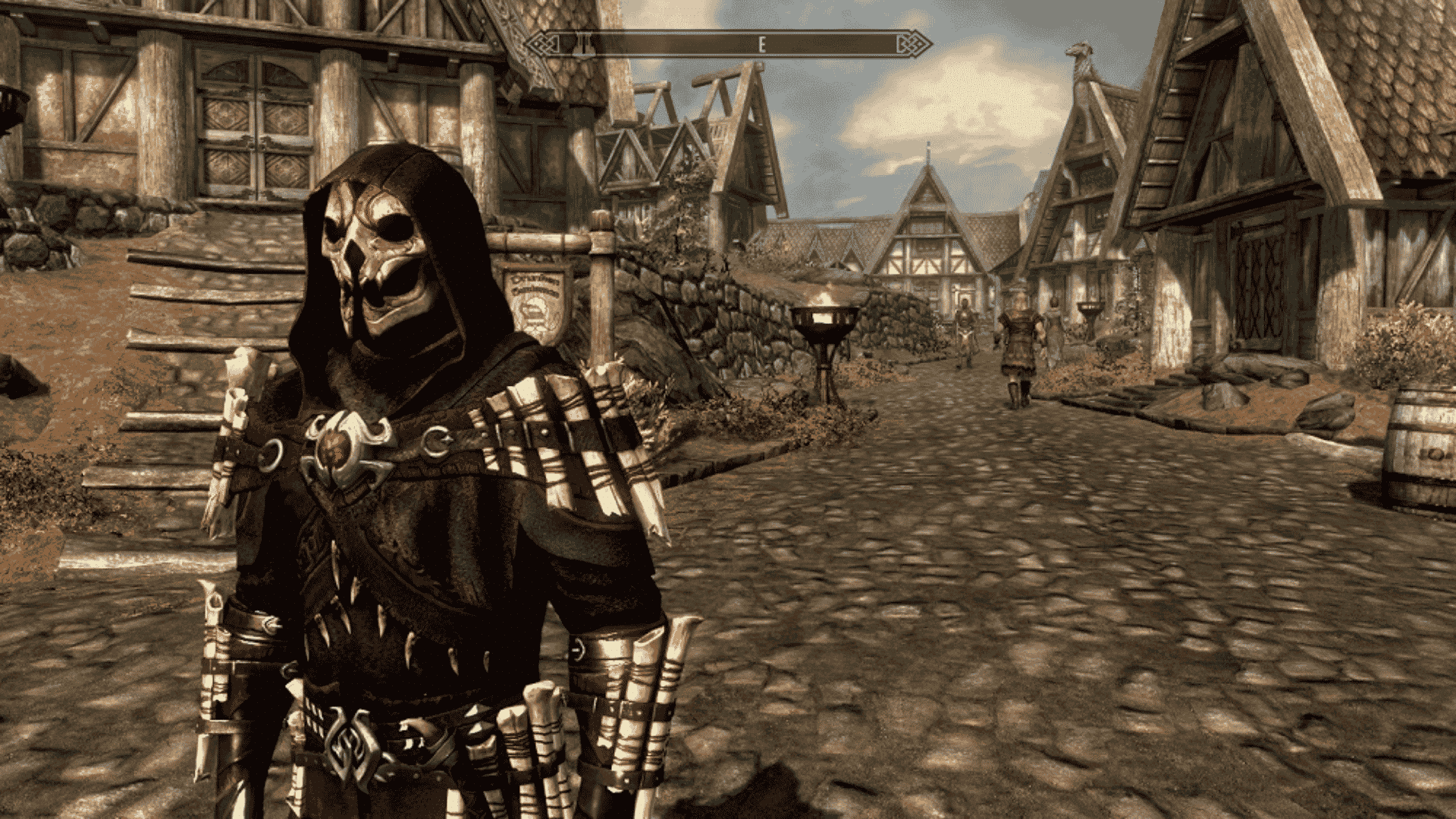 A Skyrim character wearing a hooded skull mask and armor stands on a cobblestone street in Whiterun.