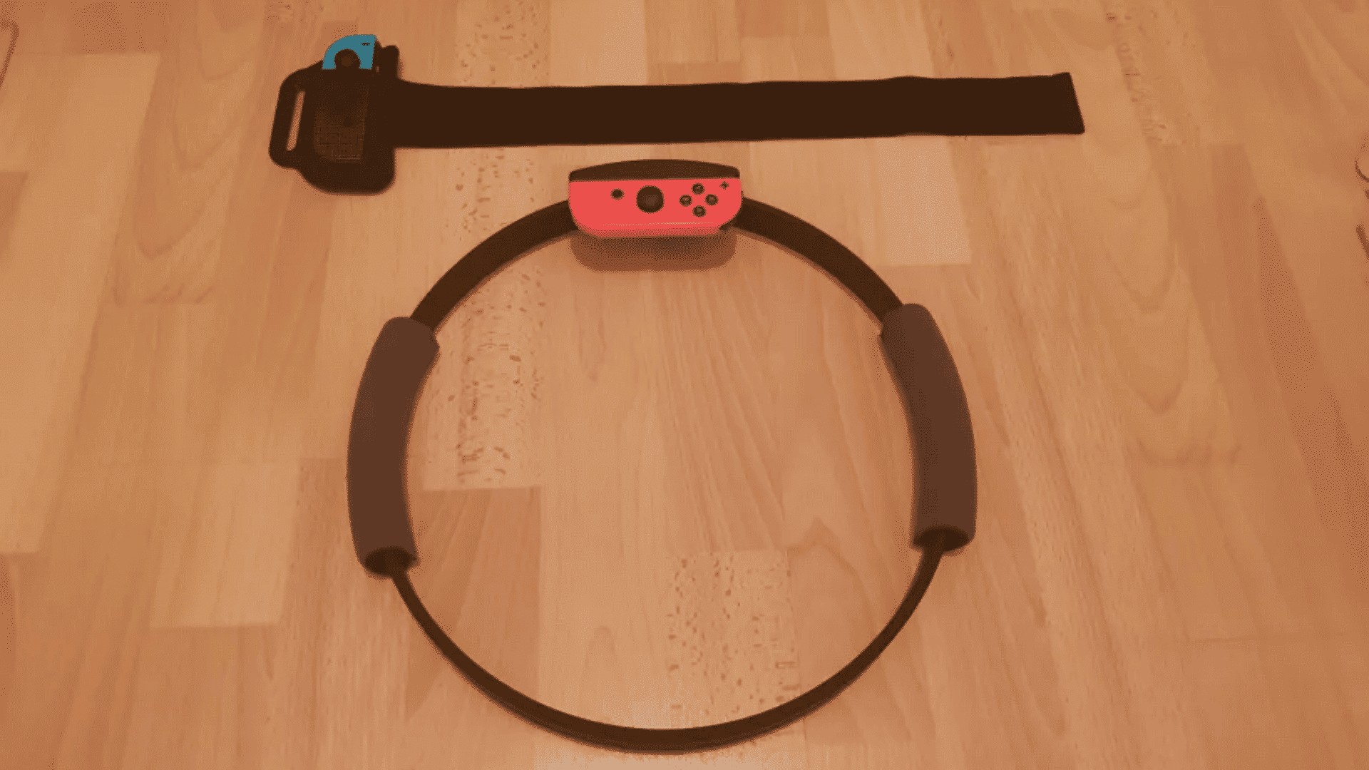 Nintendo Switch Ring-Con with a red Joy-Con attached and a black leg strap holding a blue Joy-Con on a wooden floor.