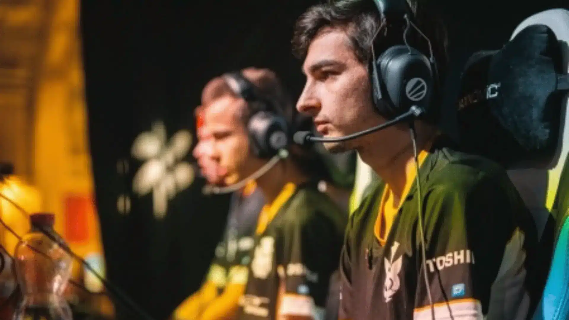 Cara, a former Rocket Leage eSports player seated at a competition setup wearing headsets, focused on gameplay on their monitors