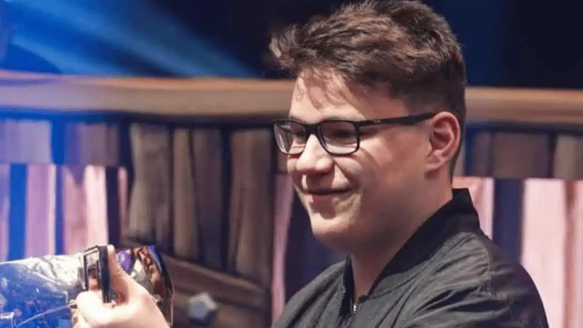 Esports player Aqua smiles while holding a trophy at a competitive gaming tournament.
