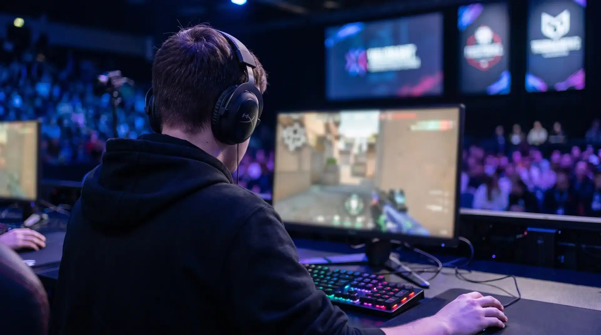 Esports player in a black hoodie wearing a headset during a gaming tournament with a blurred game screen