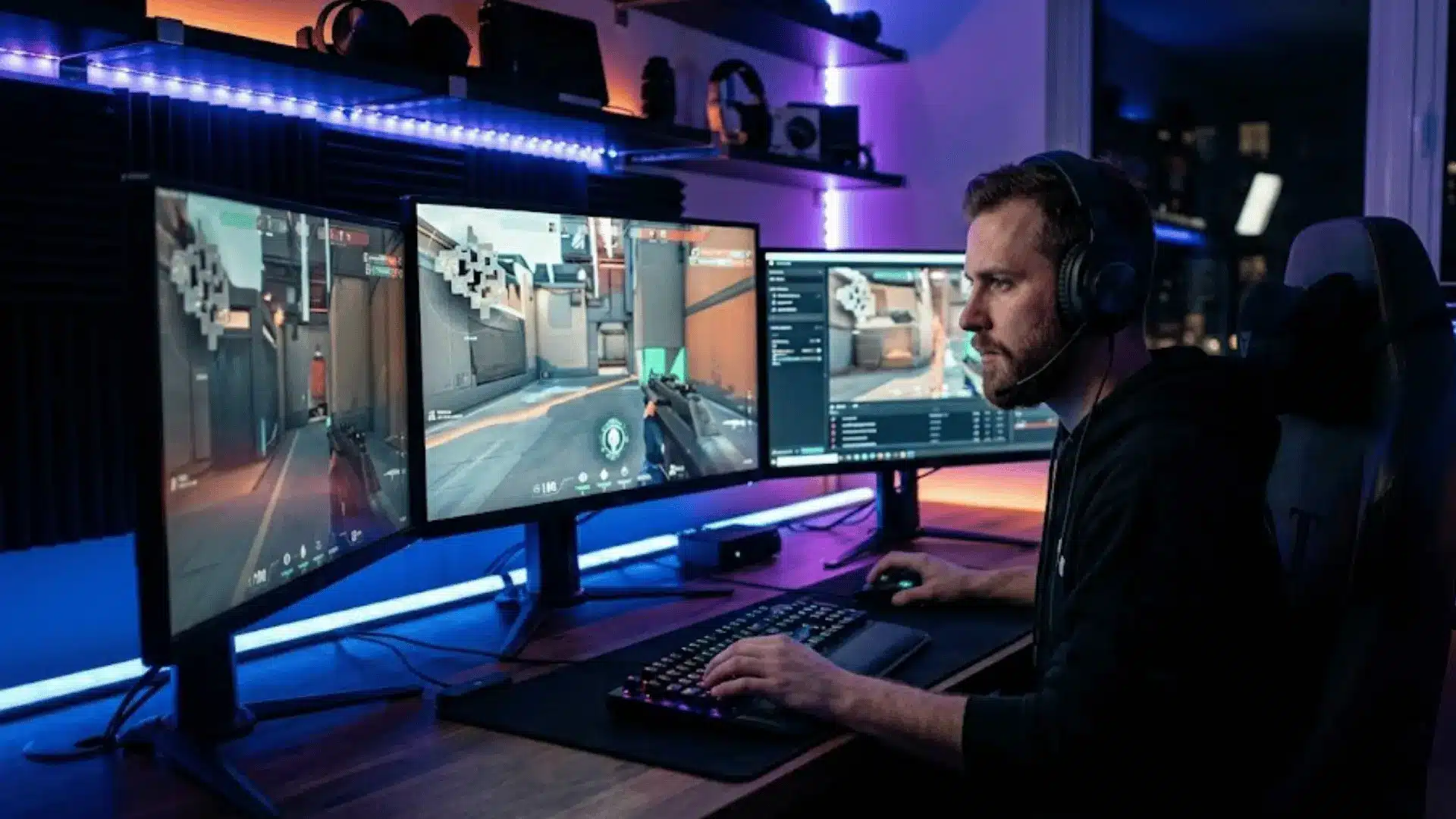 Pro gamer focused at desk playing on multi-monitor gaming setup in a dark LED-lit room.
