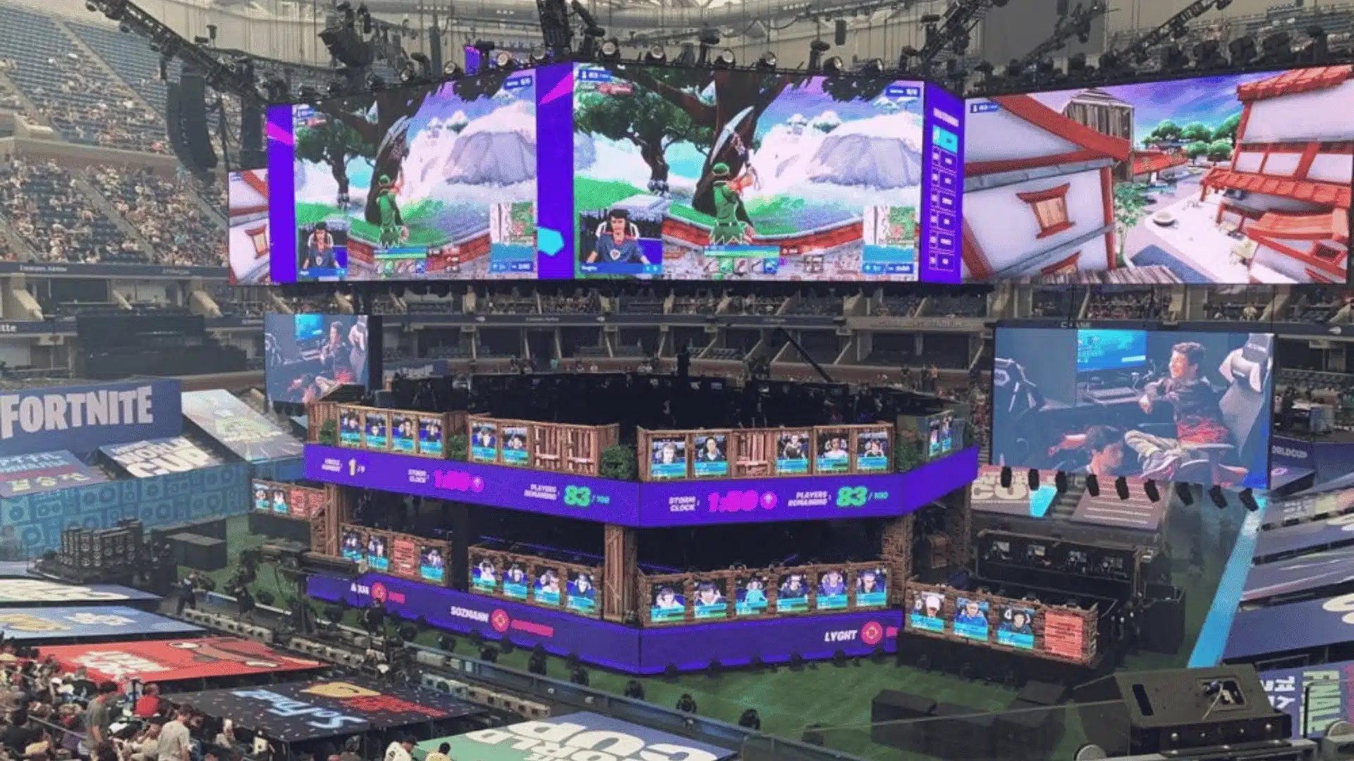 A massive stadium hosting a Fortnite esports tournament with giant video screens displaying live gameplay.