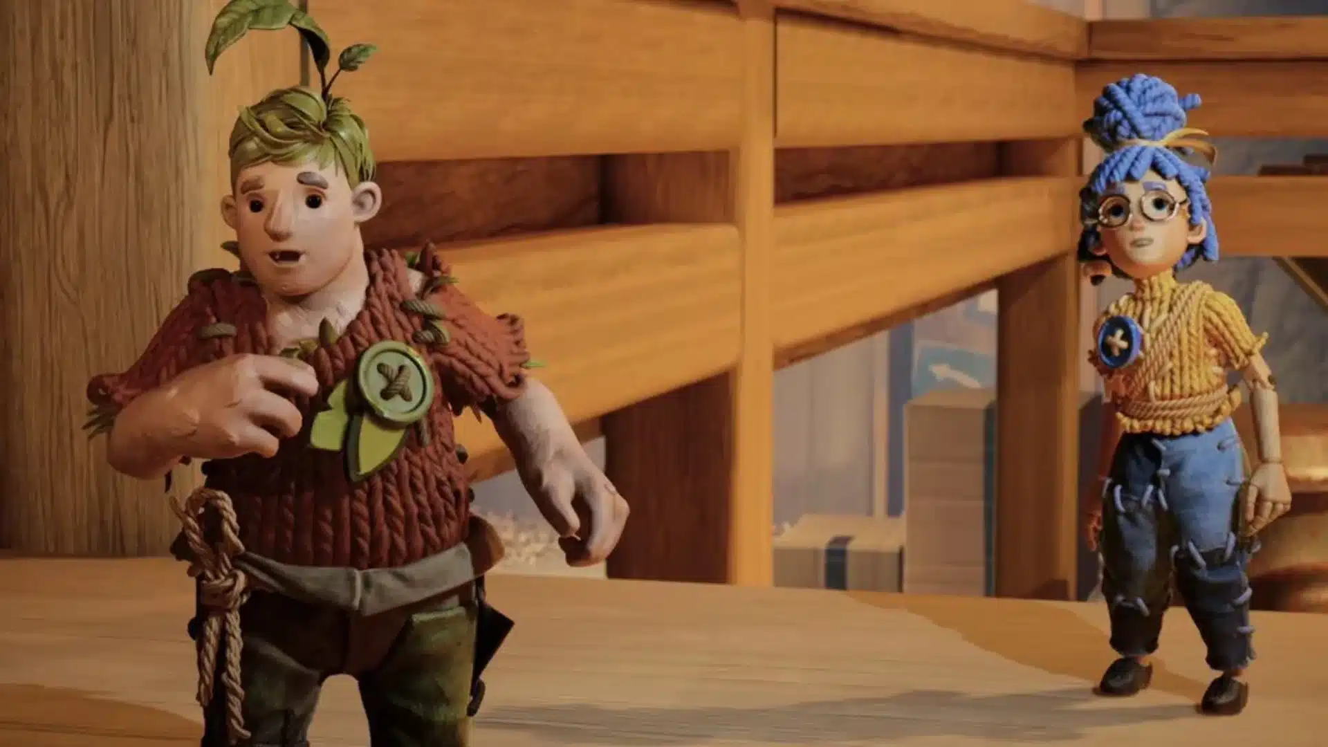 Cody and May stand on a wooden platform inside a large workshop during co-op play