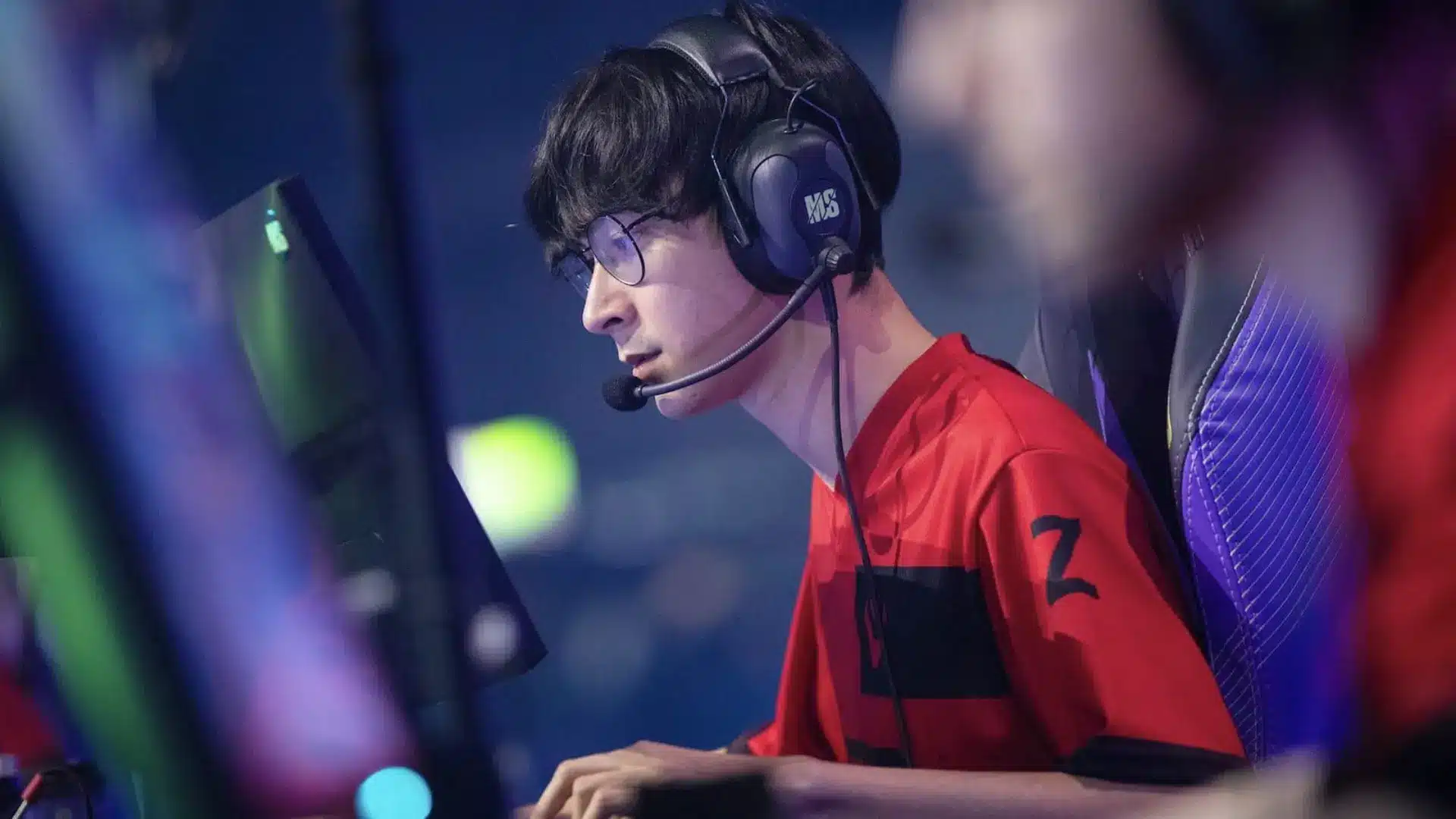 Valorant esports player wearing a headset and red jersey while playing at a gaming station