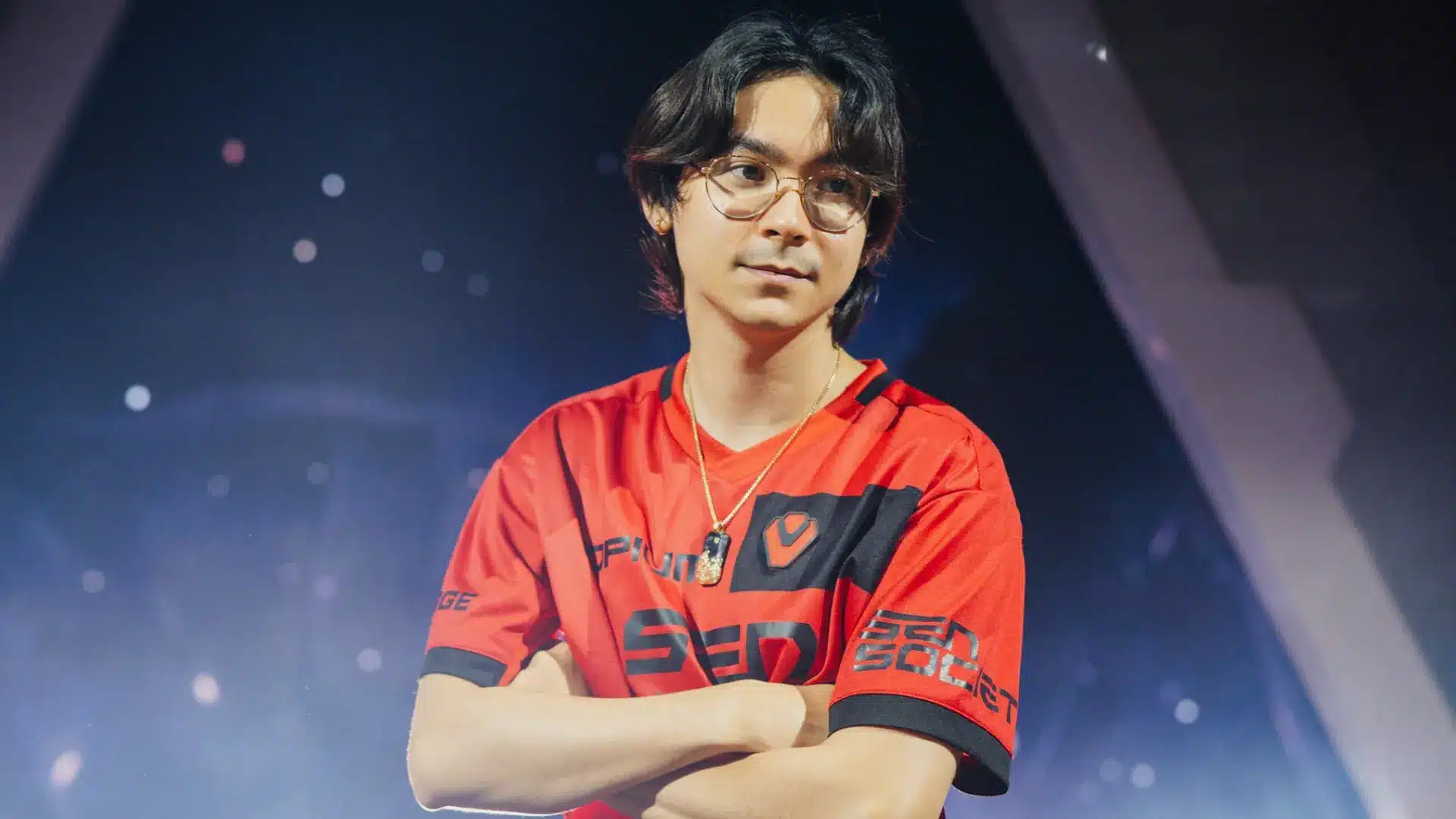 Valorant esports player in a red jersey standing on stage with arms crossed