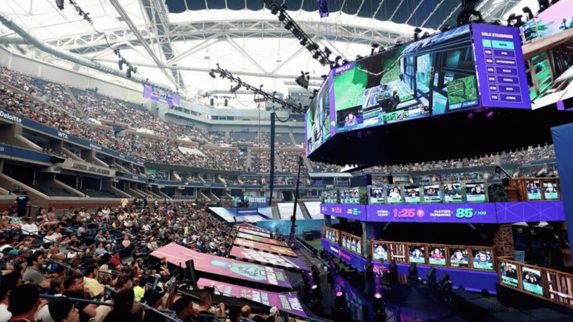 Crowded Fortnite tournament arena showing live gameplay on large screens and a packed audience watching.