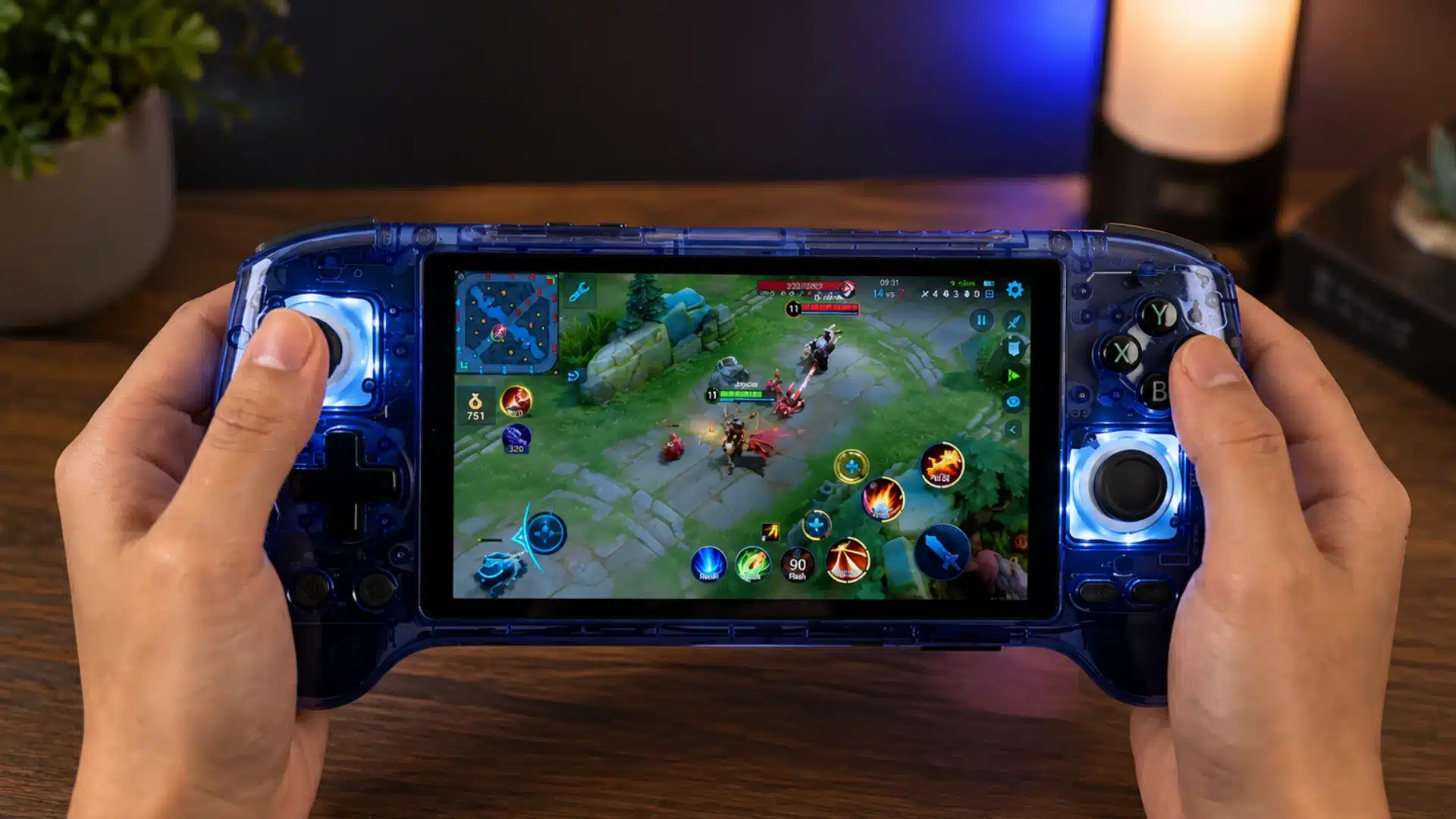 Blue transparent handheld console shows a MOBA game while held over a wooden desk