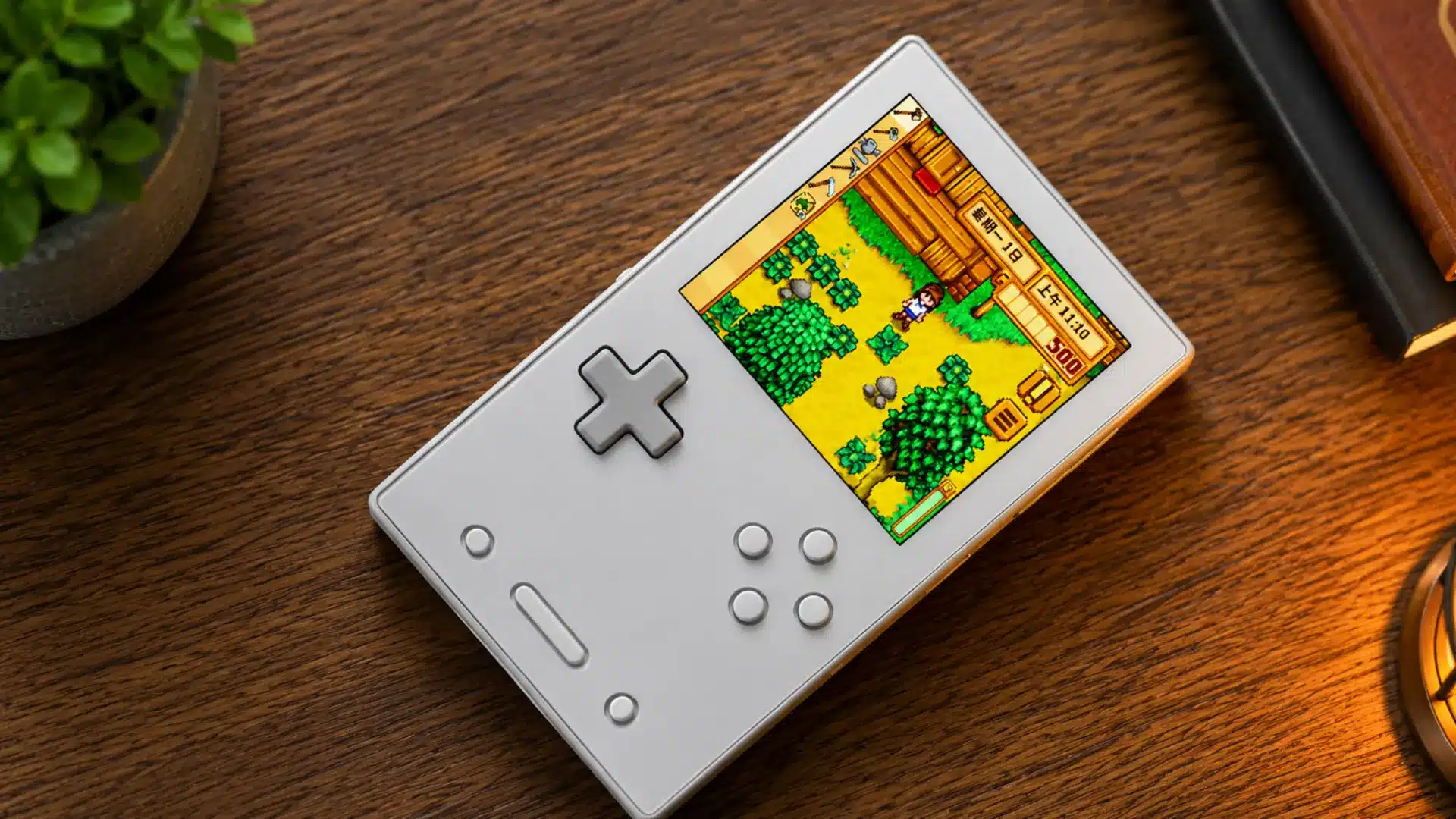 Silver retro handheld displays a colorful farming game on a warmly lit wooden desk